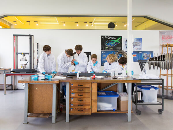 Schüler in weißen Laborkitteln stehen an einem Tisch und führen ein Experiment durch. 