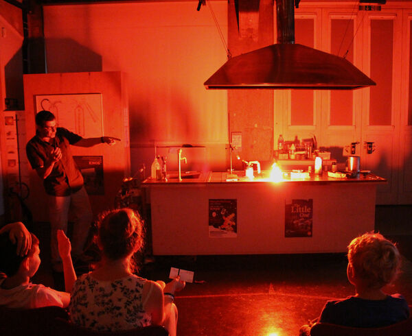 Ein Museumspädagoge führt im Feuerlabor Experimente vor einer Schulklasse vor.