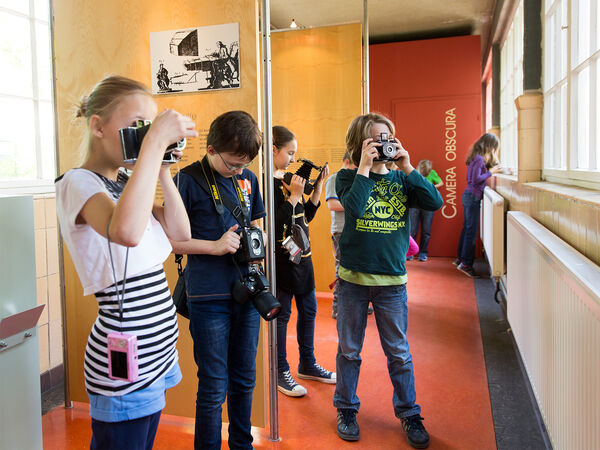 Kinder stehen vor dem Eingang zur Camera Obscura und schauen durch historische Fotoapparate und Laufbodenkameras. 